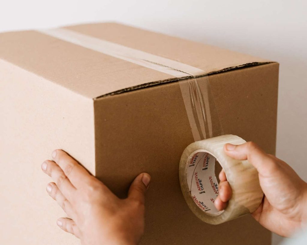 Close-up of hands applying clear adhesive tape to a cardboard package, representing the efficient fulfillment and shipping standards supported by Part n Parcel.